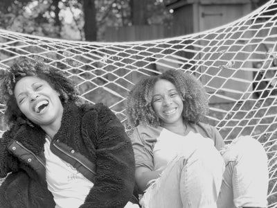 Marisa Campbell and Eliane Saint of Lifing-It Podcast laughing on a hammock. This represents the be you collection of greeting cards by beknown.
