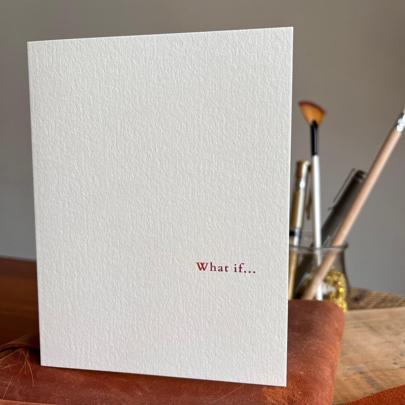 Beknown greeting card on leather notebook next to pencil holder. What if...